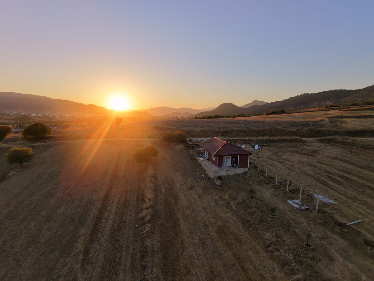 Low sun over fields and a red-roofed cabin, from a drone