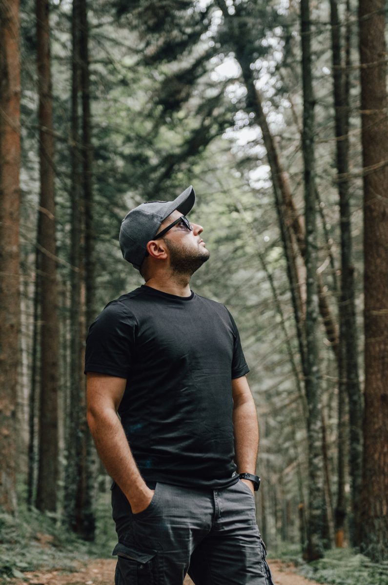 Ömer standing among tall pines, looking up