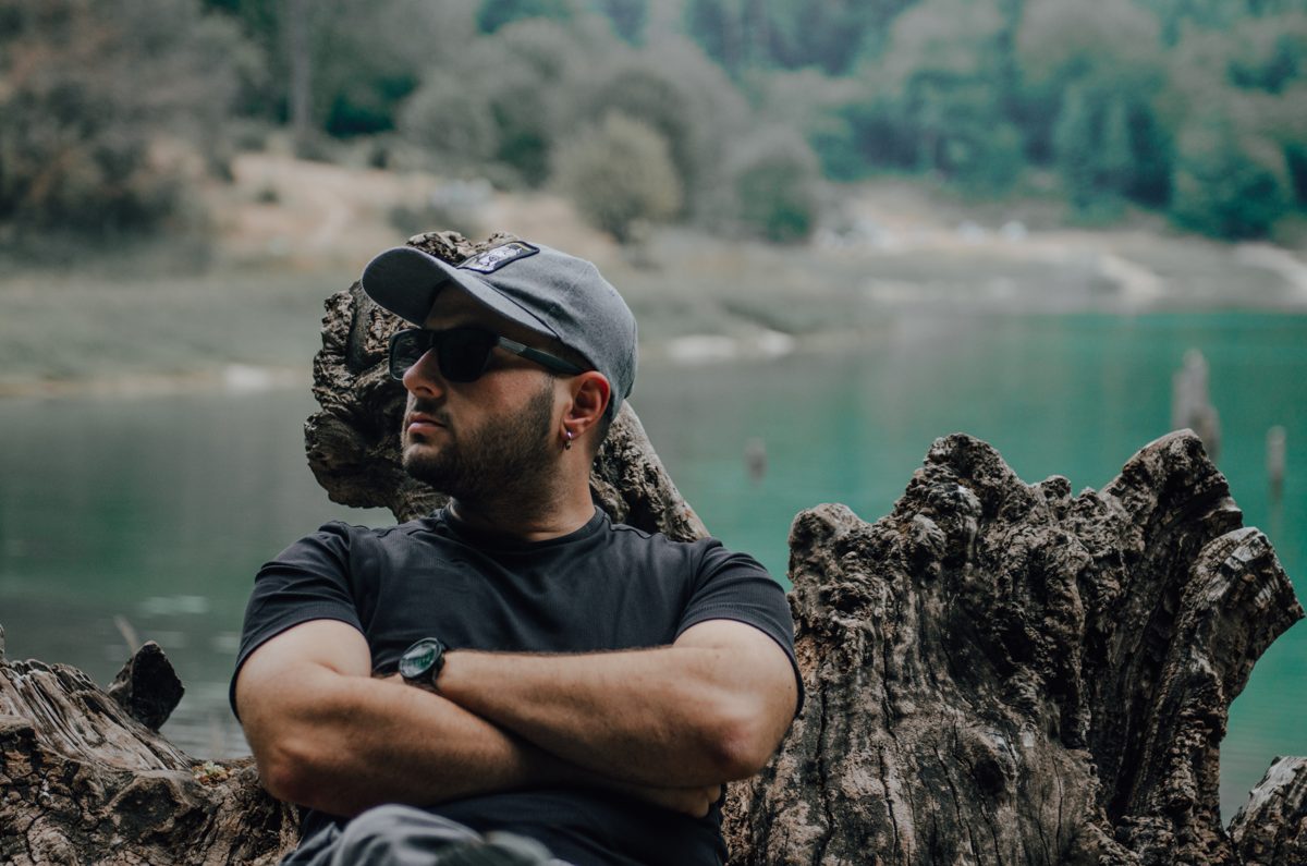 Ömer Zeyd Okumuş sitting on driftwood by a lake, arms crossed