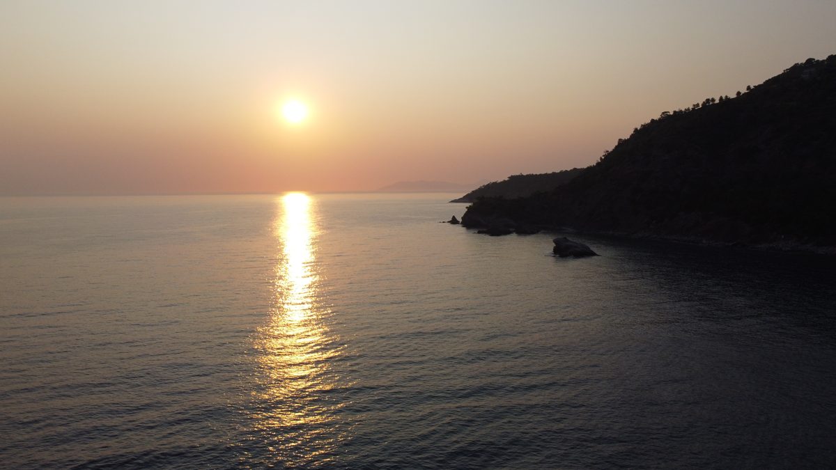 Sun setting over the sea behind a dark headland